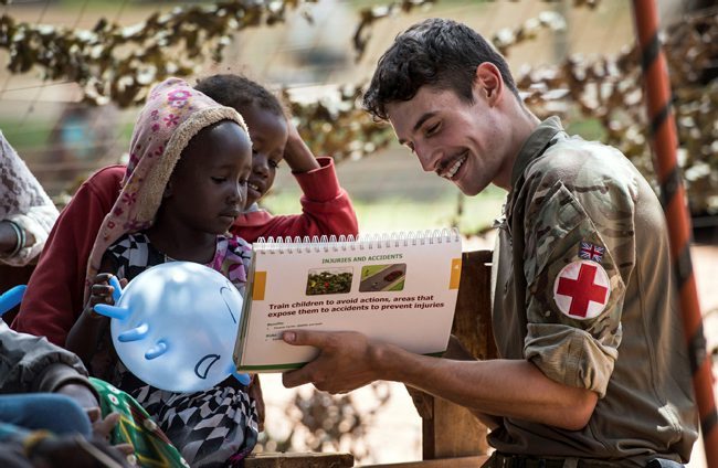 A reservist is holding up a brochure to two children in Kenya to educate them on safety.