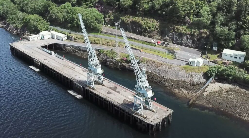 Aerial view of the previous jetty structure. There is a large area of concrete, the jetty, and two cranes.