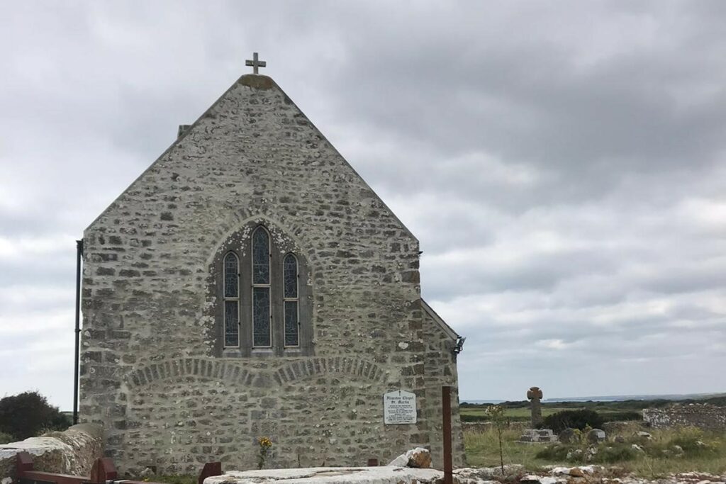 Image taken from the side of the chapel, showing the renovated brick walling. There is a stained glass window in the central part of the wall, with a cross on the top part of the roof.