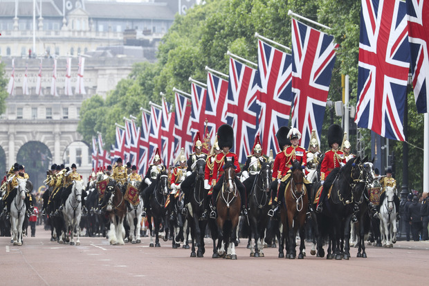 A procession of horse-mounted military personnel in decorative uniform.