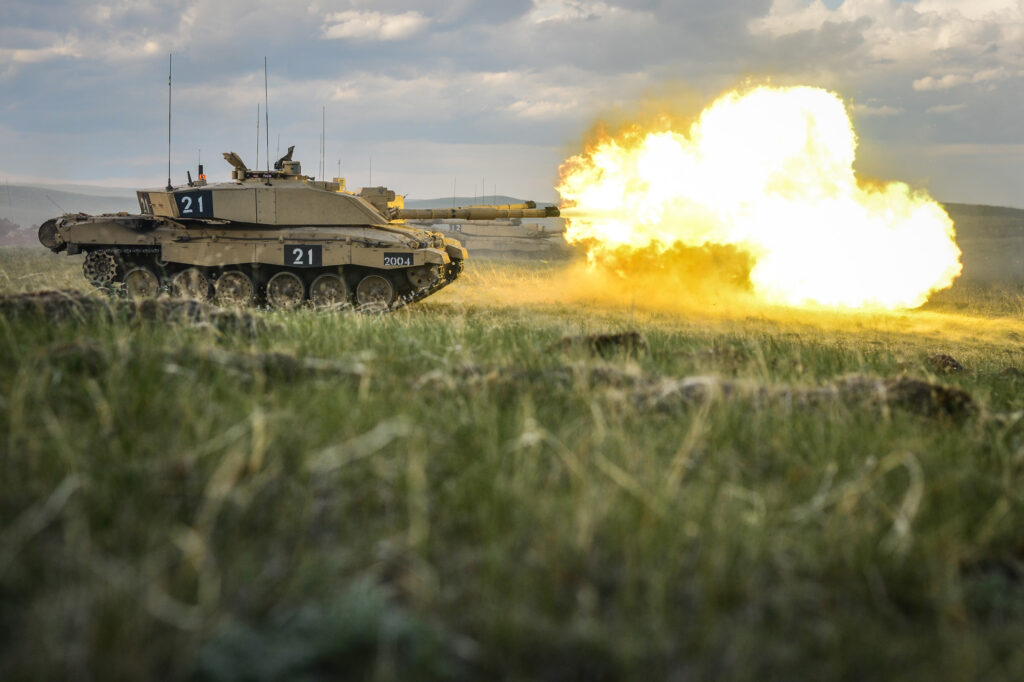 A Challenger 2 tank firing from its main turret, on a large grassy field.