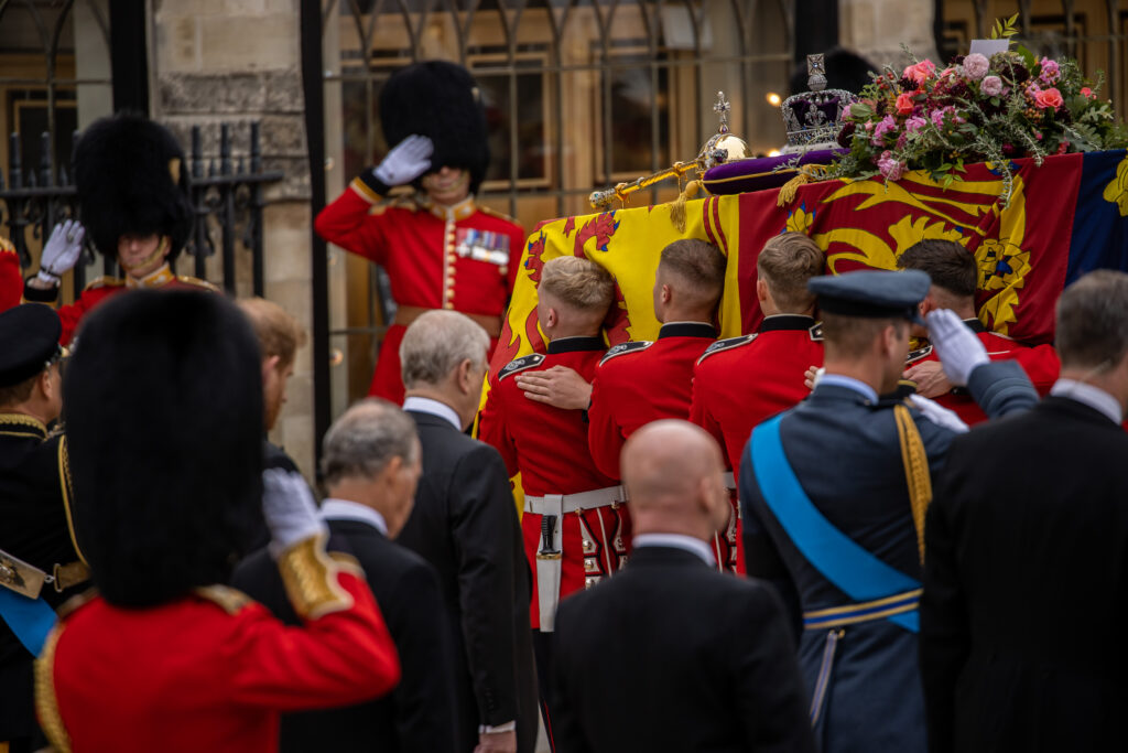 The bearer party of guardsmen, in red tunics but without their famous bearskins, carry HM The Queen's coffin, draped in the Royal Standard and topped with the Crown Jewels and a bouquet of flowers.