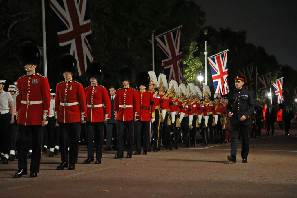 Soldiers of the Guards Division and Household Cavalry, and Royal Navy sailors, line up in the early hours of the morning. From the Union flags behind them they appear to be on The Mall. 