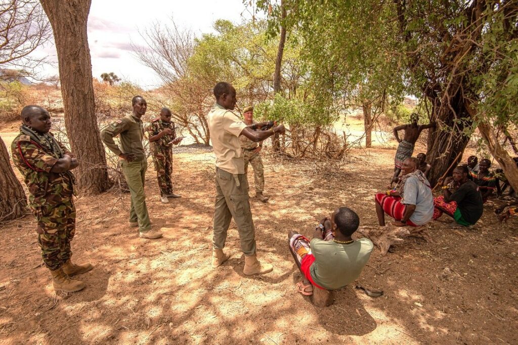 Personnel from the Kenyan Defence Forces and Sappers from 17 Field Squadron Royal Engineers sitting in the shade getting briefed on their task