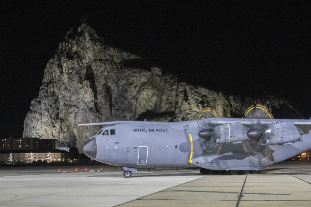 Nighttime image of the RAF Gibraltar runway, with the Rock of Gibraltar behind and slightly lit up. On the runway is a large grey RAF aircraft, an A400M.