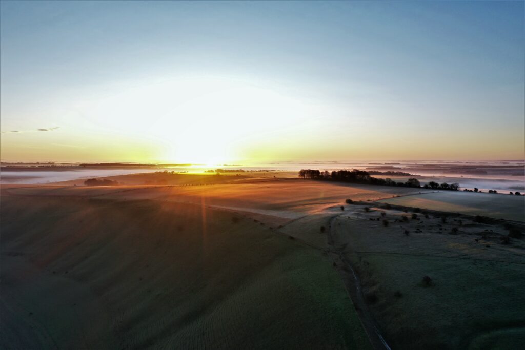 Aerial view of a sunrise over Salisbury Plain. There is little light to illuminate the land but the sky is starting to light up. 