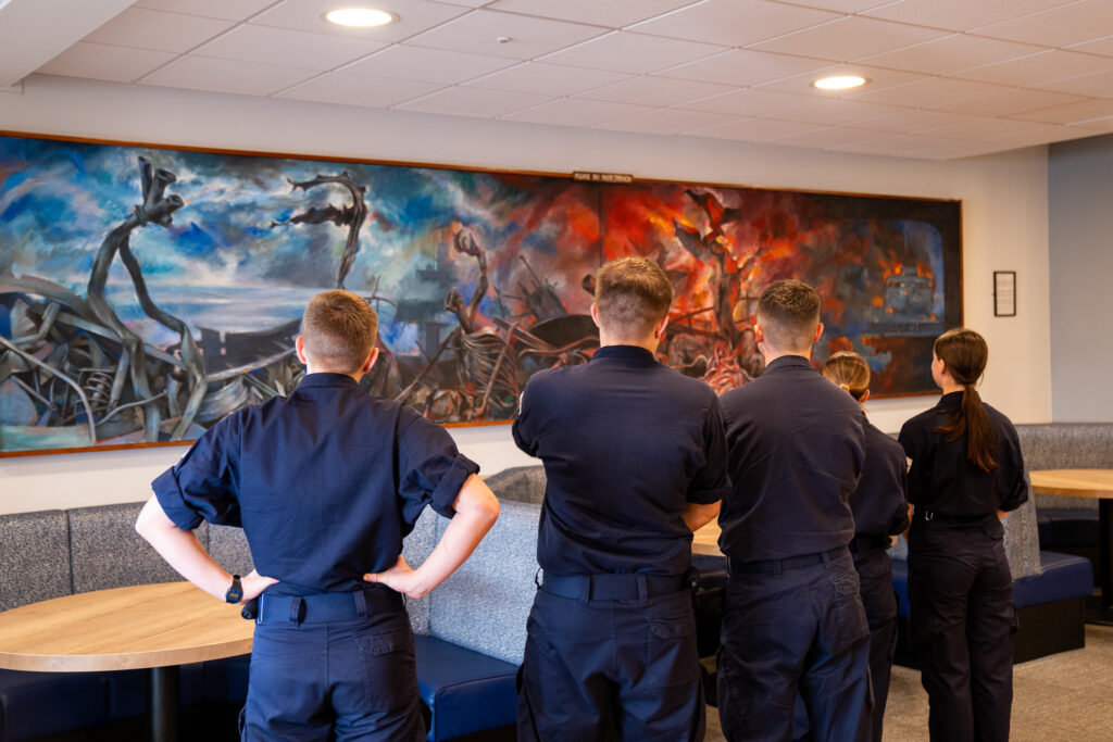 Naval recruits in uniform are seen from behind looking at a striking painting depicting the Falklands War. The abstract image features blues and oranges as it show the Bluff Cove air attacks in June 1982.