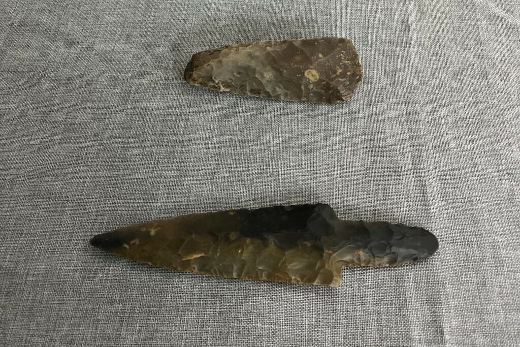 Archaeological finds arranged on a piece of cloth. At the bottom is a pointed flint object with a handle and at the top is what looks like a flint knife. 