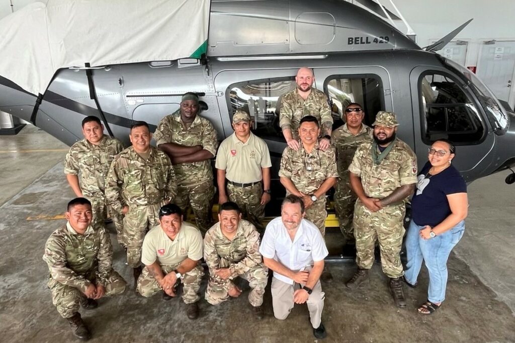 A group of thirteen people, mostly wearing military uniform, pose in front of a helicopter.