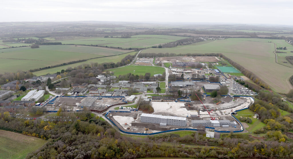 A number of buildings are located in Worthy Down with green fields and trees surrounding it.