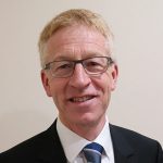 Head and shoulders image of Graham Dalton, a white man with fair hair and glasses, wearing a suit and tie. He is smiling.