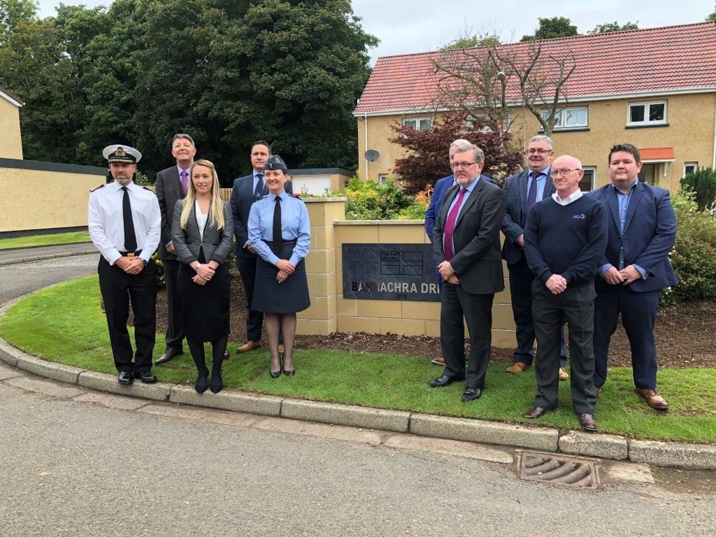 Wendy Rothery, Craig Mearns, David Mundell and others pose by a sign reading "Bannachra" in front of some of the refurbished homes.