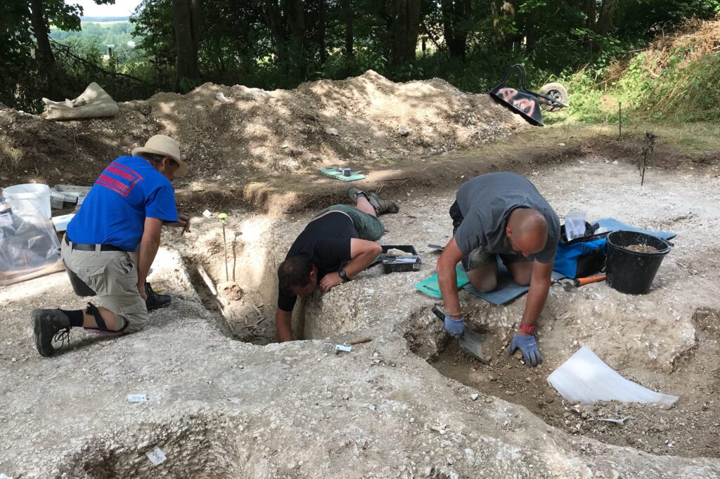 Three participants kneeling on the ground next to an archaeological trench, taking part in an Op Nightingale dig.