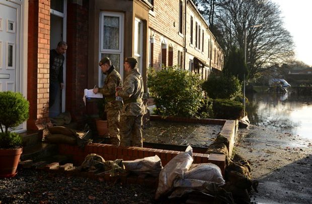 Two soldiers from 2 LANCS speaking to a homeowner in a flooded street.