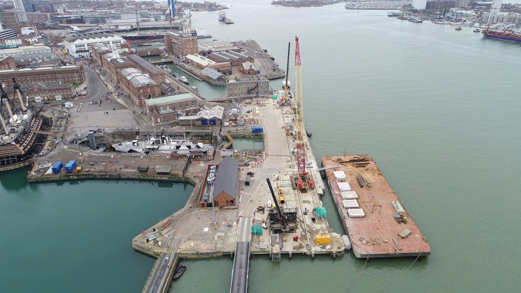 A aerial view of construction work taking place at HMNB Portsmouth. Image shows the sea, cranes and buildings.