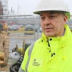 Project Manager, Colin Efford is pictured in a hi-vis jacket and helmet. Behind him is construction work taking place at HMNB Portsmouth