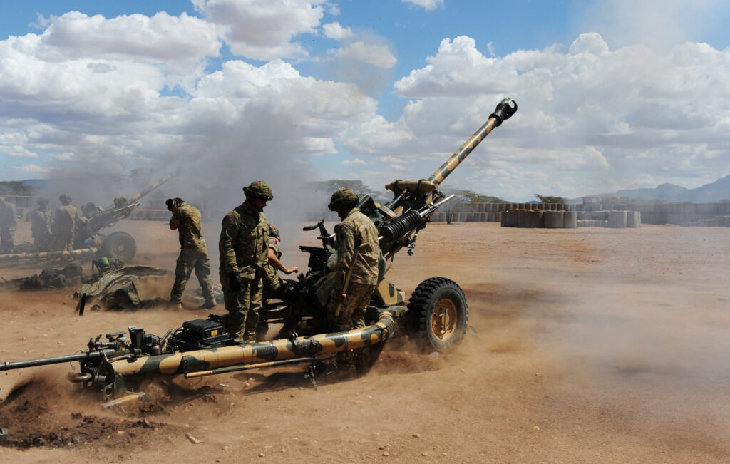 Soldiers from 4 RIFLES firing artillery on exercise in Kenya. The ground is red and dusty.