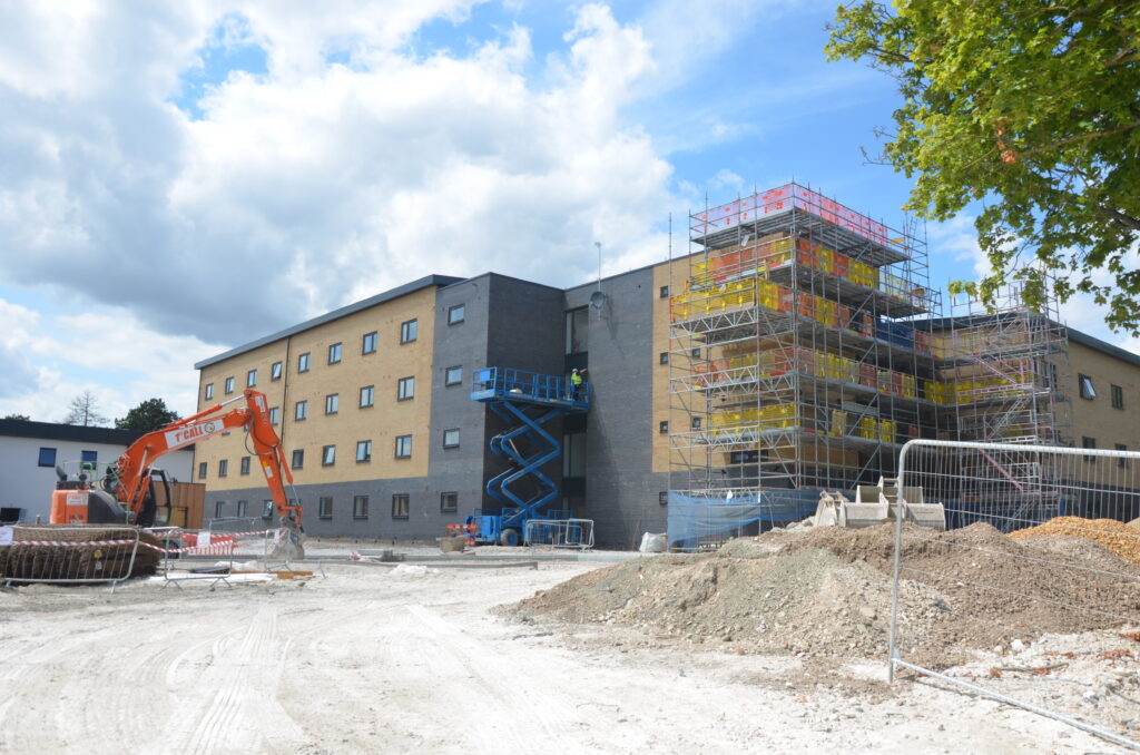 A service family accomodation block is pictured in coloured bricks and grey under construction. Pictured is an orange track next to it.