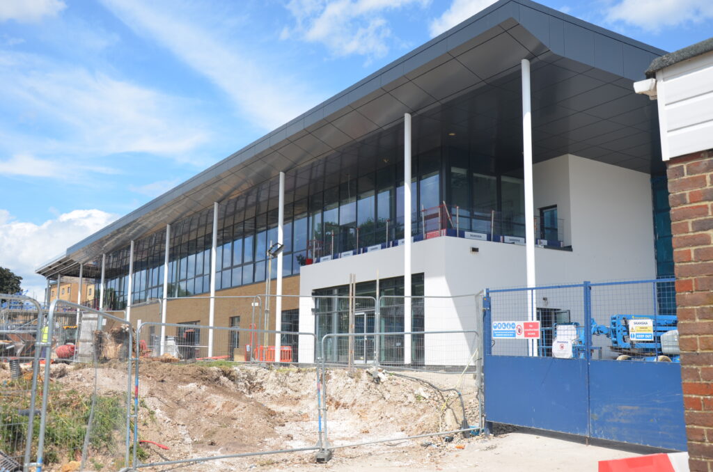 Pictured is a white and grey building with several windows under construction. The building is a new officers' and senior commissioned officers' combined mess at Worthy Down. There is grey fencing infront of the building and soil