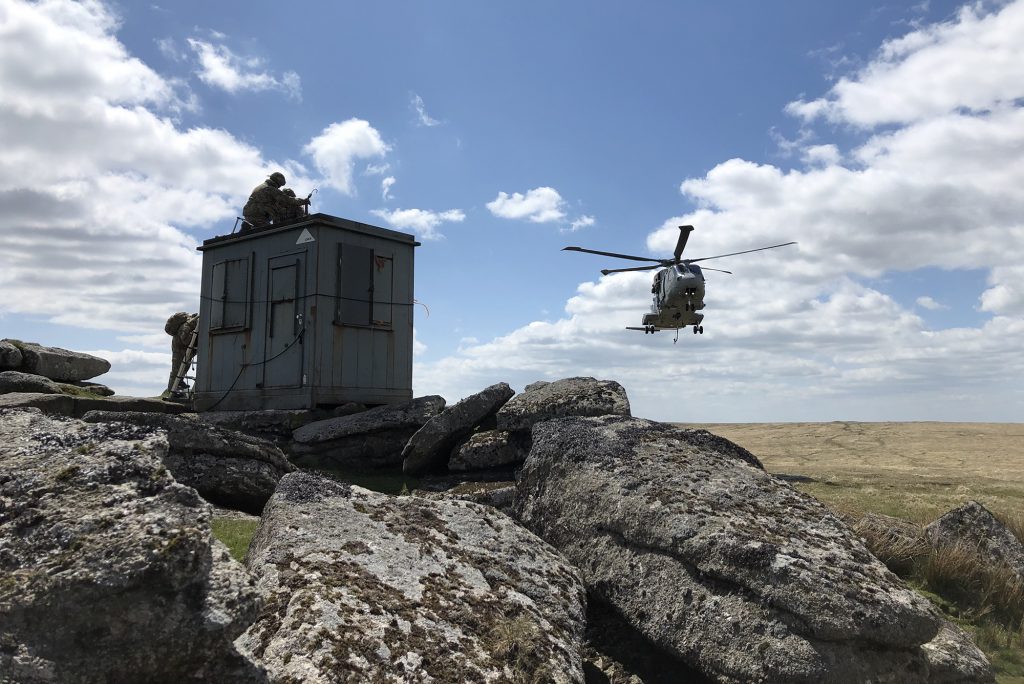 A Range Clearance hut sits on a rocky outcrop with a helicopter approaching from the rear.