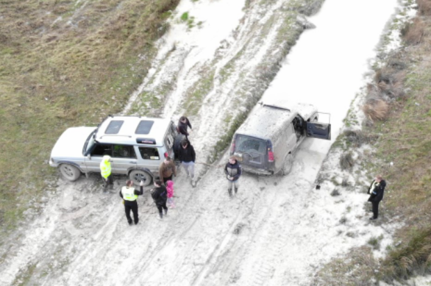 An aerial view from the drone of MOD Police officers talking to the drivers of two parked 4x4 vehicles. 