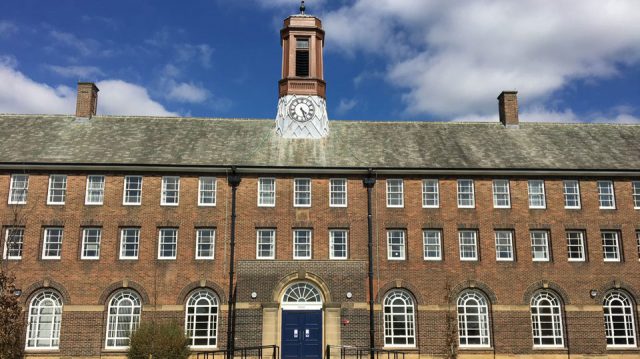 The Sandhurst Block is a grade II historic building with an old brown brick look and clock with roman numerals in the middle of it. It was refurbished to represent a modern look inside but keep the historic features of the building.