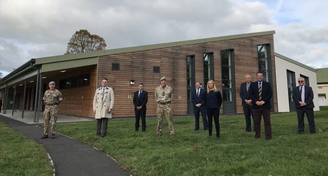 9 representatives from DIO, Landmarc and Pave aways are stood on grass infront of the new facility which is a brown woooded building with long window panels and green roofing.