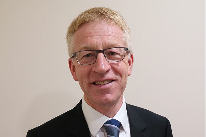 Graham Dalton, DIO's Chief Executive. Graham is a white man with light hair and glasses, wearing a black suit, white shirt and striped tie. He is smiling.