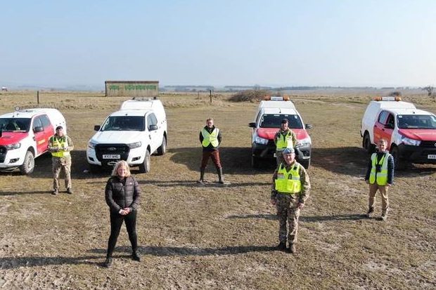 Lucy standing outside with members of the training estate team and four vehicles on an open plain. The image is taken from a drone so is from a little way in the air.