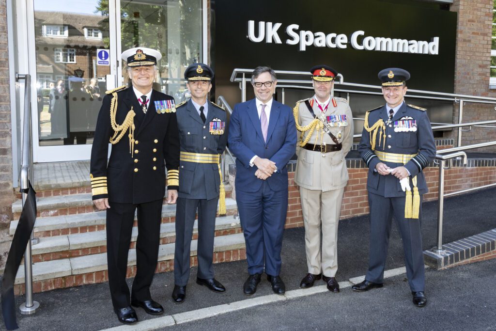 Five men standing outside the UK Space Command HQ. One is in a blue suit, one in naval uniform, two in RAF uniform and one in Army uniform.