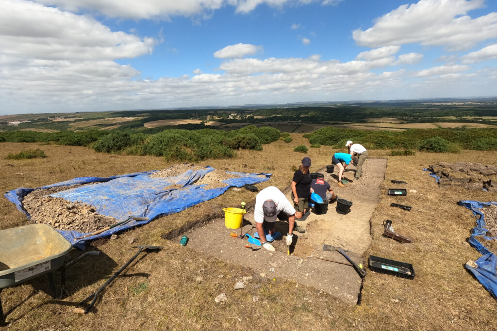 A view looking down onto participants kneeling and excavating a trench with the expanse of the training area in the background.