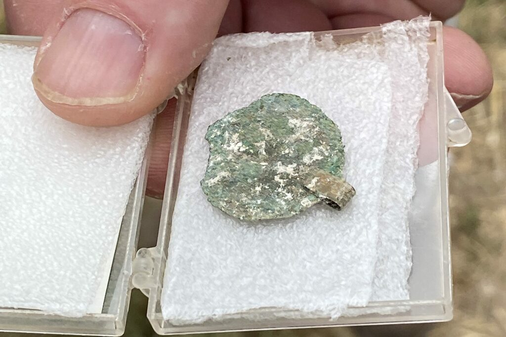 A hand holding a small flat disc, carefully placed in a transparent plastic display box.