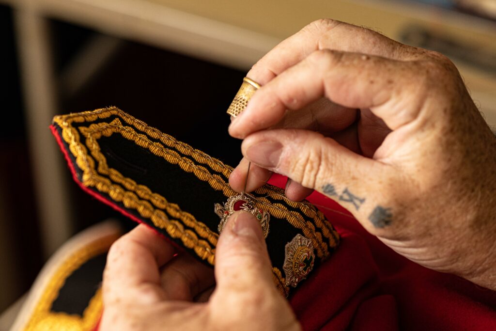 A close up of two hands sewing the shoulder badge on a red tunic of the Guards Division. 