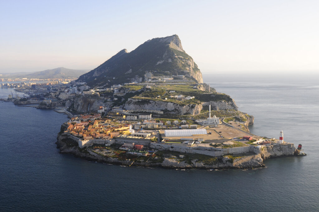 Aerial view of Gibraltar, surrounded by sea on three sides. The Rock forms the backdrop with buildings in the foreground to the end of the headland.