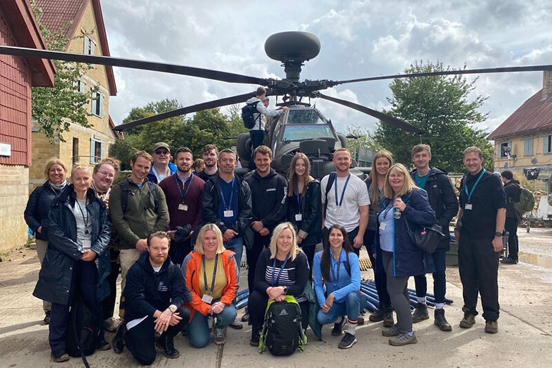 A group photo of DIO apprentices stood in front of an Apache helicopter.