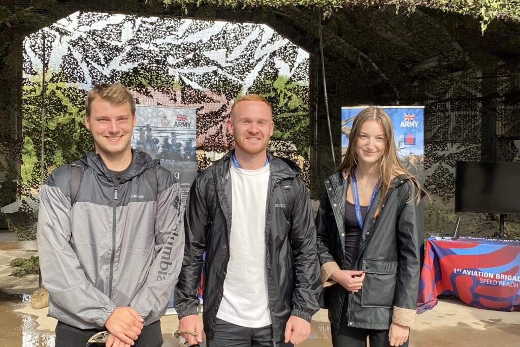 A group photo of two male apprentices and a female apprentice, stood in front of a display stand at the Army Expo 22.