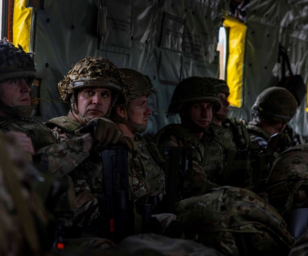 Several men in military uniform sit in the back of a vehicle