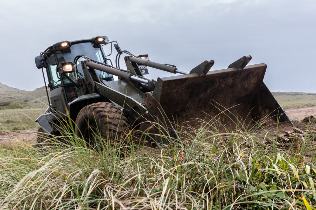 A military digger moving soil and scrub 