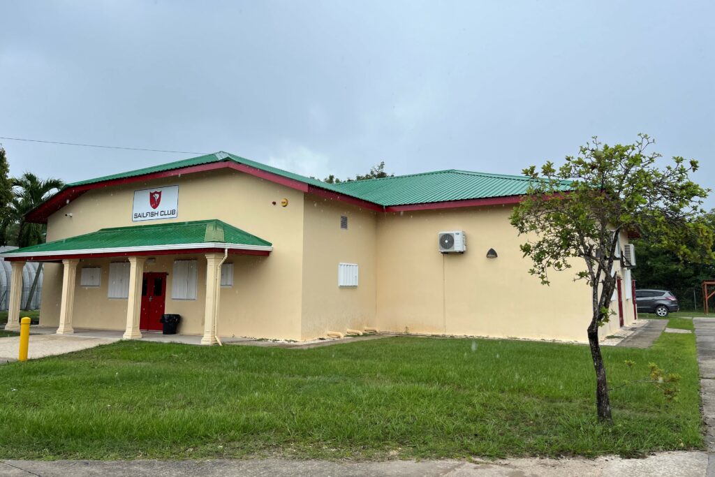 The Sailfish Club, a single-story building with cream-coloured brickwork and a sloped green roof. In front of it is a grass lawn.