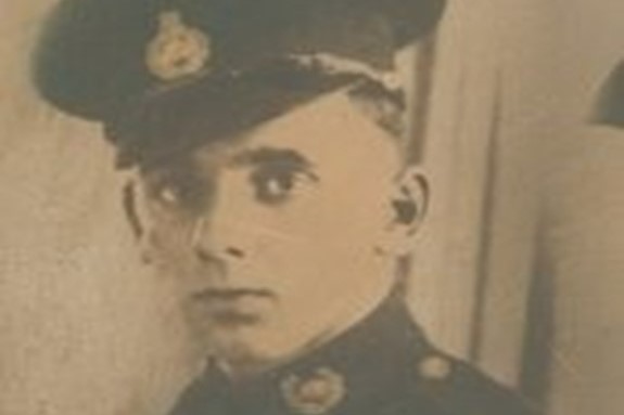 A sepia-toned image of a young man in military uniform and a black badged hat.