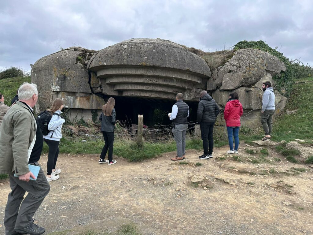 A group of people in casual clothes looking at a concrete bunker resembling the mouth of a cave.