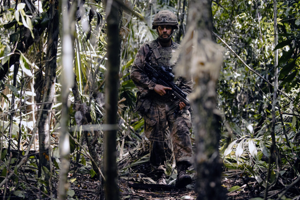 A soldier walks towards the camera through the jungle.