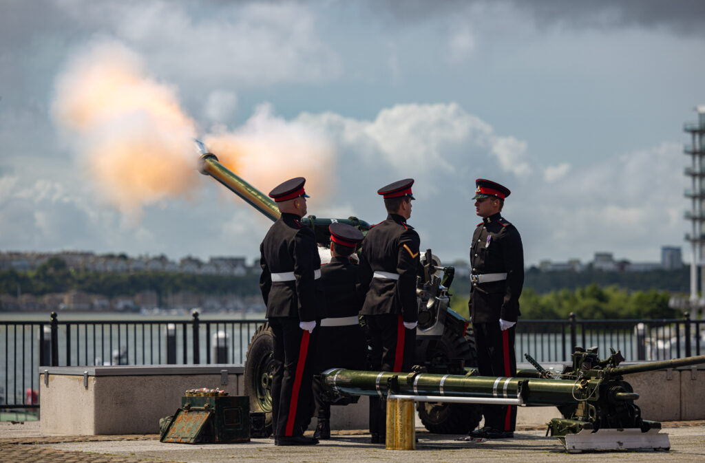 Four soldiers in uniform fire an artillery gun over the water.