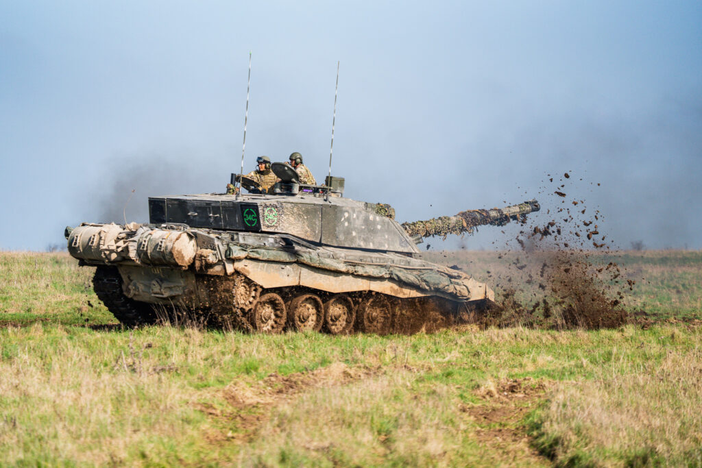 A Challenger 2 tank reversing and kicking up mud from the front.